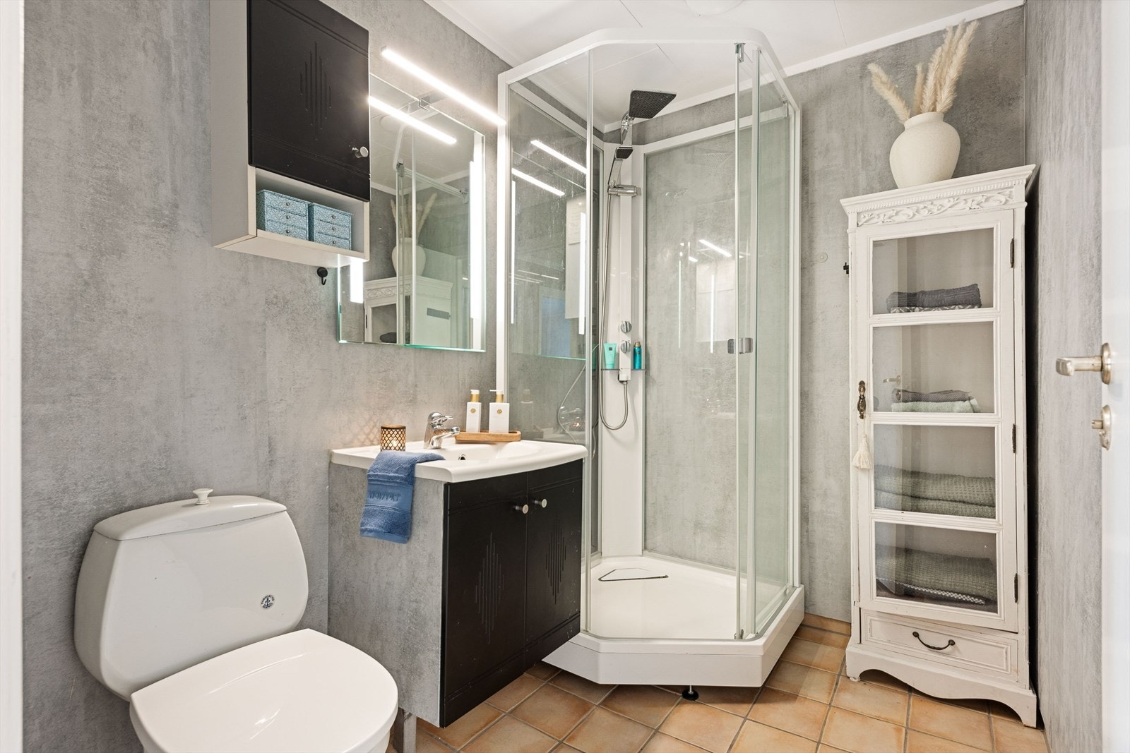 Baderom med fliser og varmekabler i gulv. Rommet er utstyrt med servant over skapinnredning, speil med belysning, dusjkabinett og toalett Galleribilde