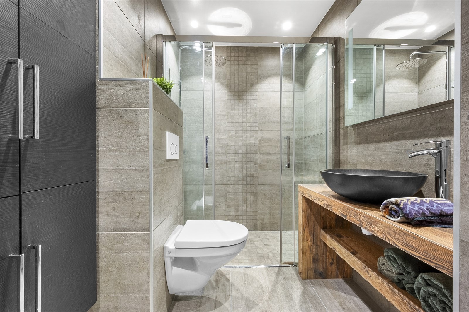 Innredet med vegghengt toalett, servant på innredning, speilskap og dusjhjørne med skyvbare glassdører. Galleribilde