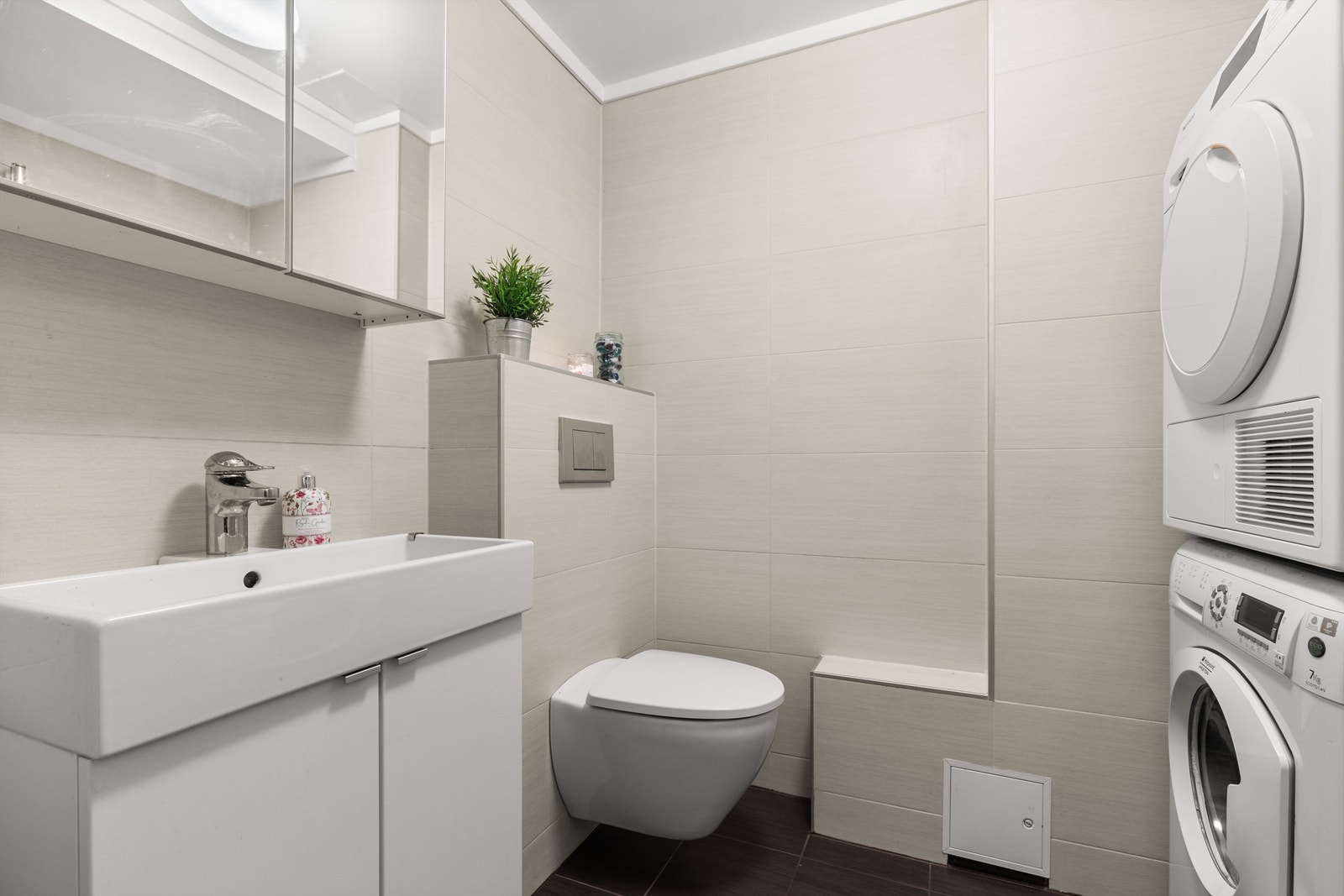 Badet i 1. etasje er flislagt på gulv og vegger med varme i gulvene, og er innredet med vegghengt toalett, servant med servantskap og vegghengt speilskap. Det er også opplegg for vaskemaskin. Galleribilde