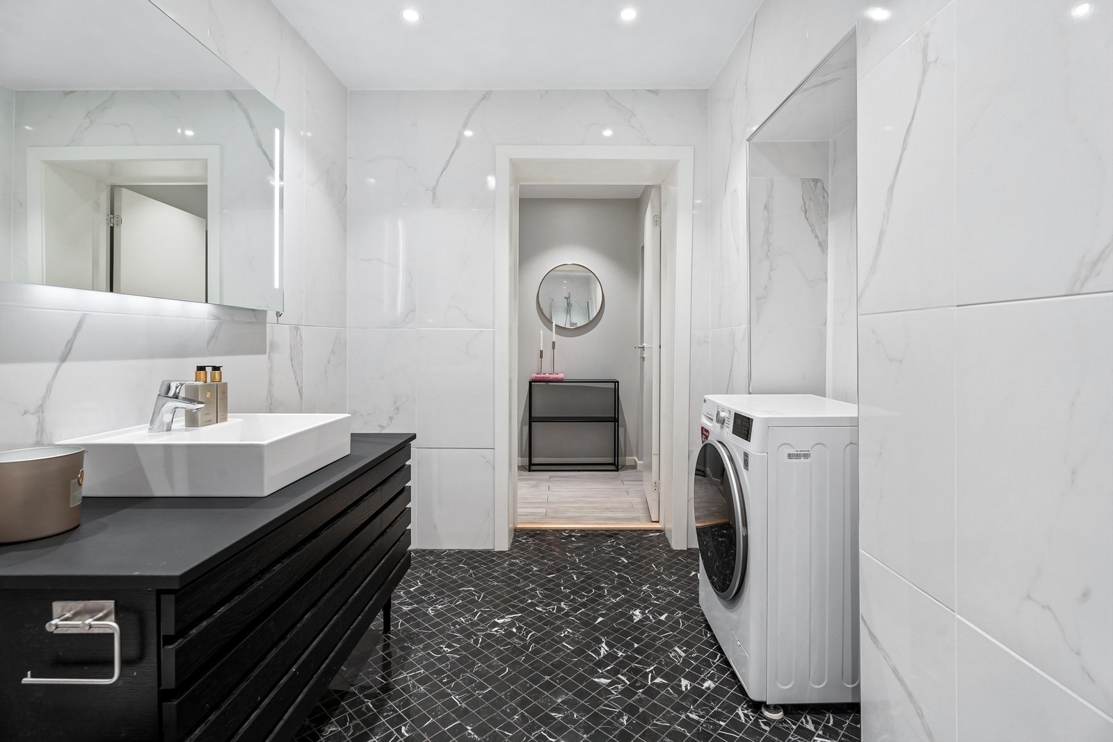 Baderom fra 2019 med opplegg for vaskemaskin, flislagte gulv med gulvvarme, flislagte vegger og nedsenket himling med downlights. Galleribilde