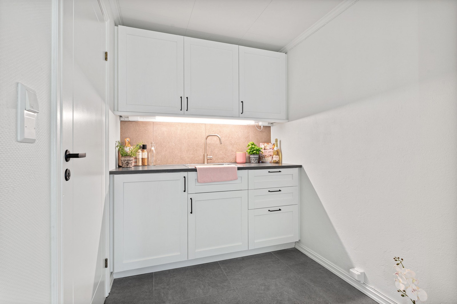 Videre er det benkeplate med laminat, oppvaskkum, fliser over benkeplate og to doble stikkontakter under overskap, samt opplegg/kontakt for komfyr og kjøleskap. Galleribilde