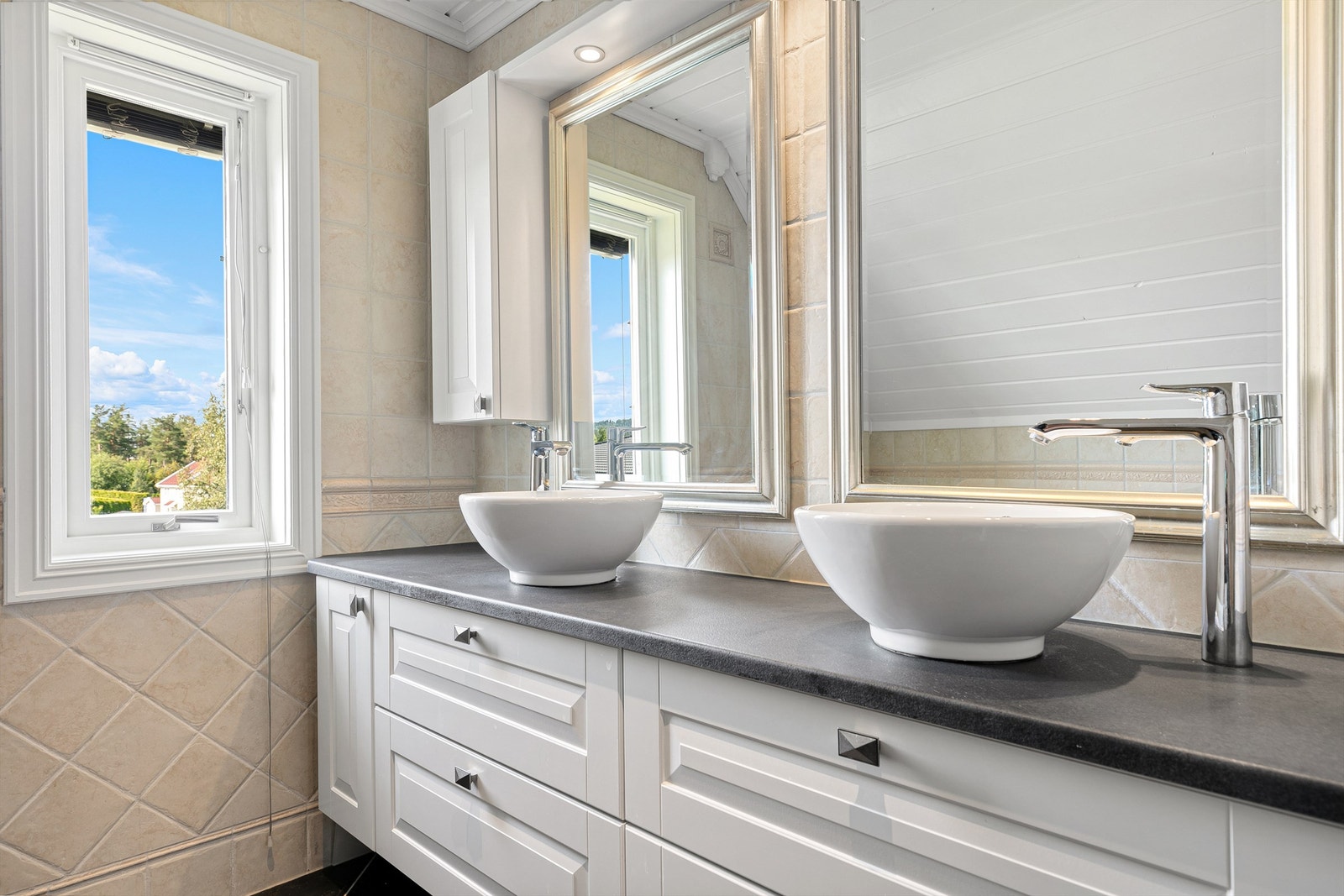 Badet fremstår som stilfullt og moderne, med profilert baderomsinnredning, to ovenpåliggende servanter og speil med overbelysning. Galleribilde