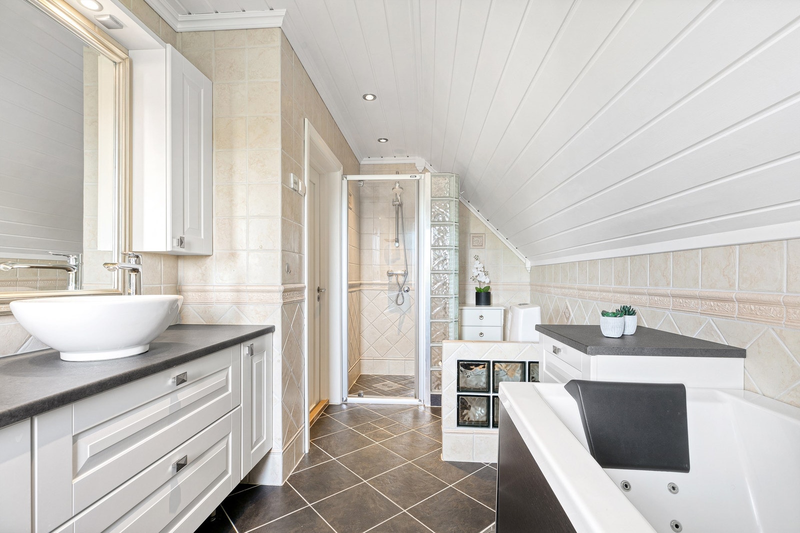 Videre er det en dusjnisje med glassdør og vegg av glassbyggerstein, massasjebadekar og frittstående toalett. Galleribilde