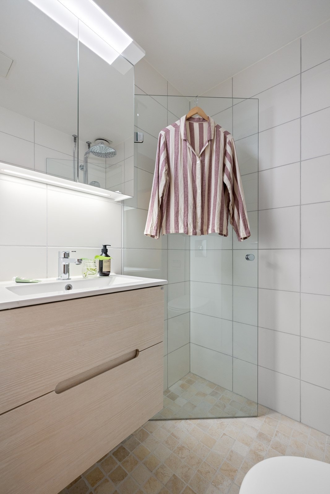 Badet er utstyrt med dusjhjørne med innfellbare dusjdører med blandebatteri med to dusjhoder, veggmontert toalett, servantskap med skuffer og hvit servant med blandebatteri. Galleribilde