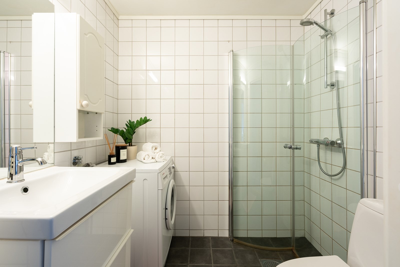 Flislagt bad med dusjnisje og innfellbare dusjdører, servant med ett greps blandebatteri og gulvstående toalett. Galleribilde