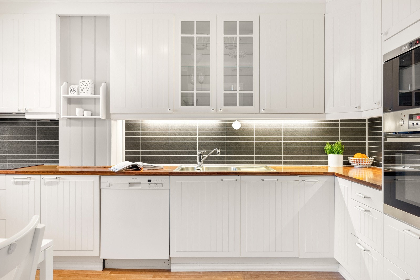 Kjøkkenet er innredet med profilerte fronter, ett glasskap og laminat benkeplate med nedfelt vask av stål. Galleribilde