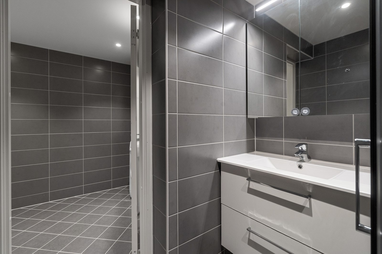 Innredningen består av dusj på gulv med dører i herdet glass, veggfestet klosett med innebygget sisterne, servant, benkeskap med glatte fronter samt overskap med speilfronter. Galleribilde