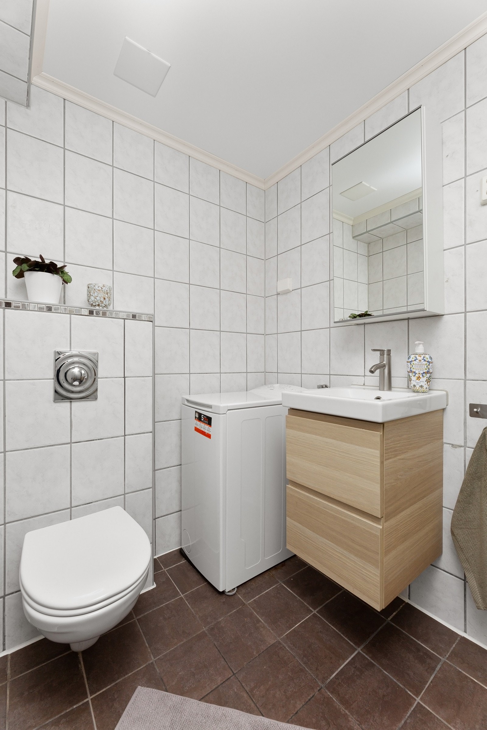 Videre er badet utstyrt med innredning med nedfelt servant, veggmontert toalett, dusjvegger/hjørne og opplegg for vaskemaskin. Galleribilde