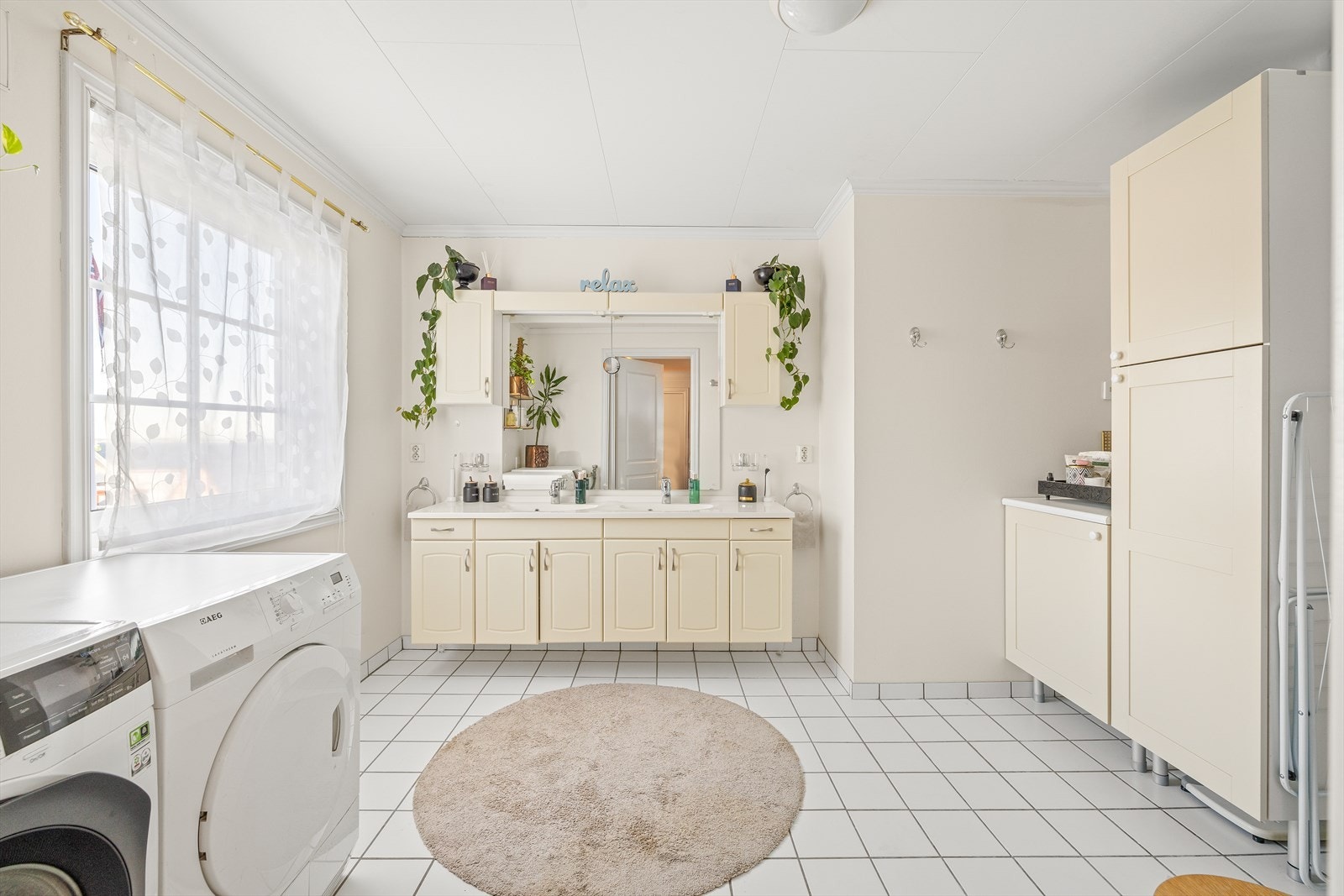 Flislagt bad / vaskerom med varmekabler som er
innredet med servantinnredning med dobbel
servant, skap, dusjhjørne, opplegg for
vaskemaskin/tørketrommel og toalett. Galleribilde