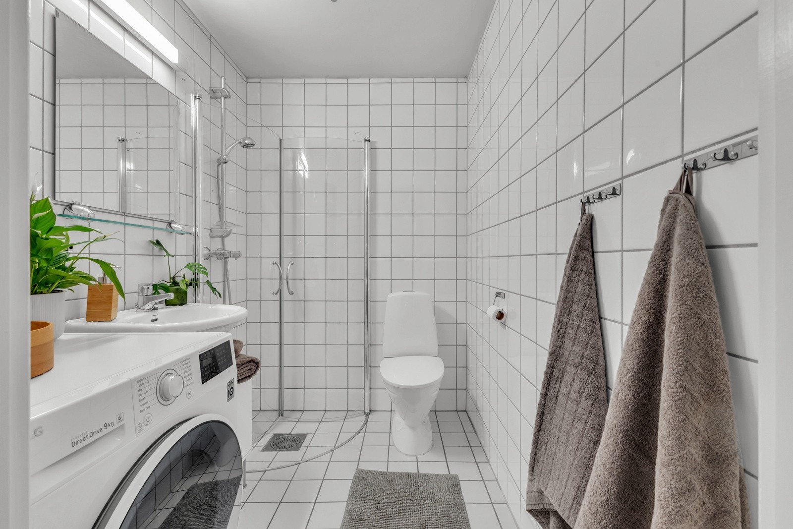 Tidløst baderom fra byggeår. Badet består av dusjhjørne med to skyvbare glassdører, gulvstående toalett, servant av porselen og opplegg for vaskemaskin. Galleribilde