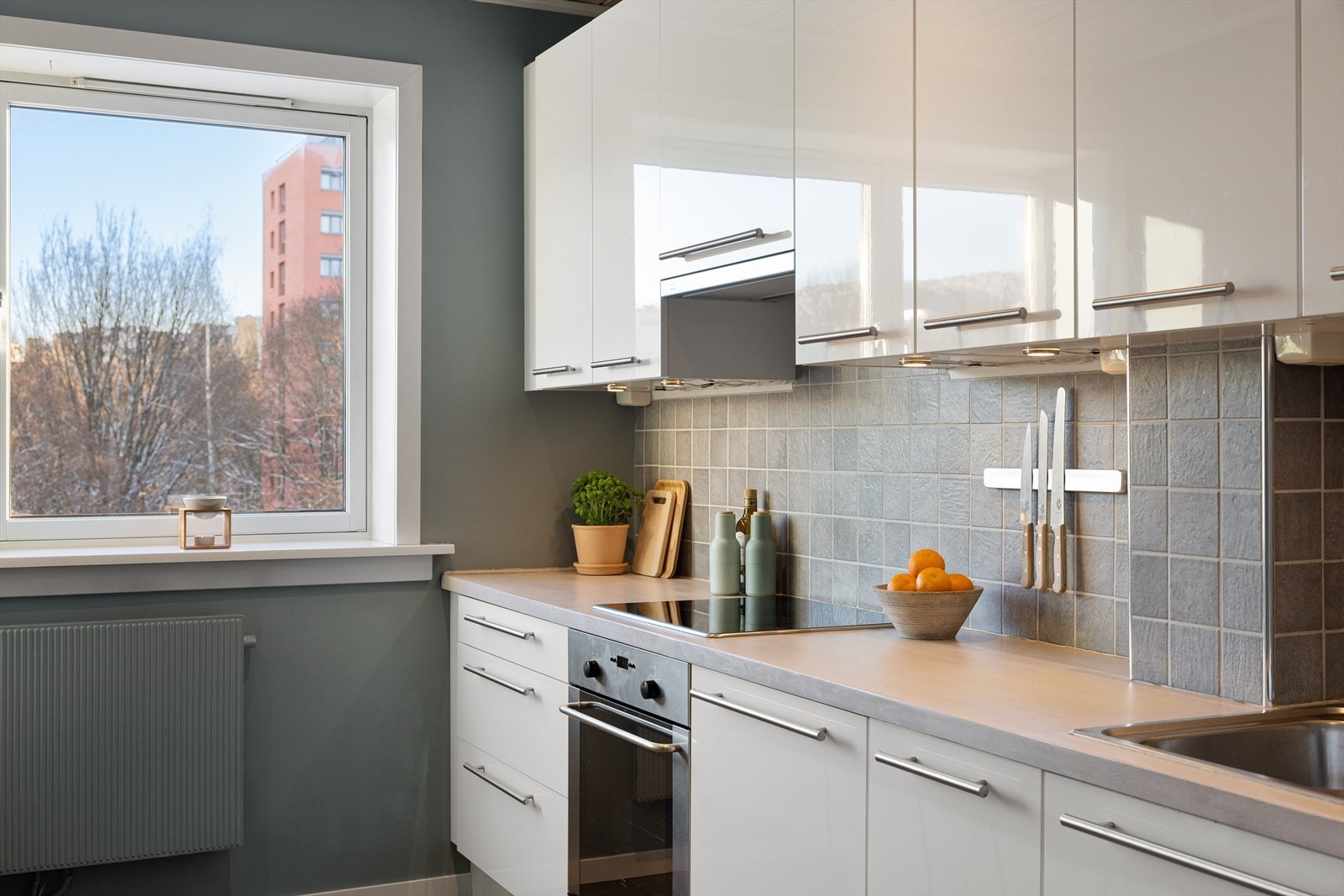 Kjøkkeninnredningen har høyglansfronter, en heltre benkeplate med nedfelt kum, og fliser på vegg over benken. Galleribilde