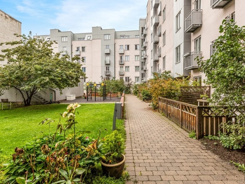 Frodig gårdsrom med sittegrupper, lekestativ og grill. Galleribilde