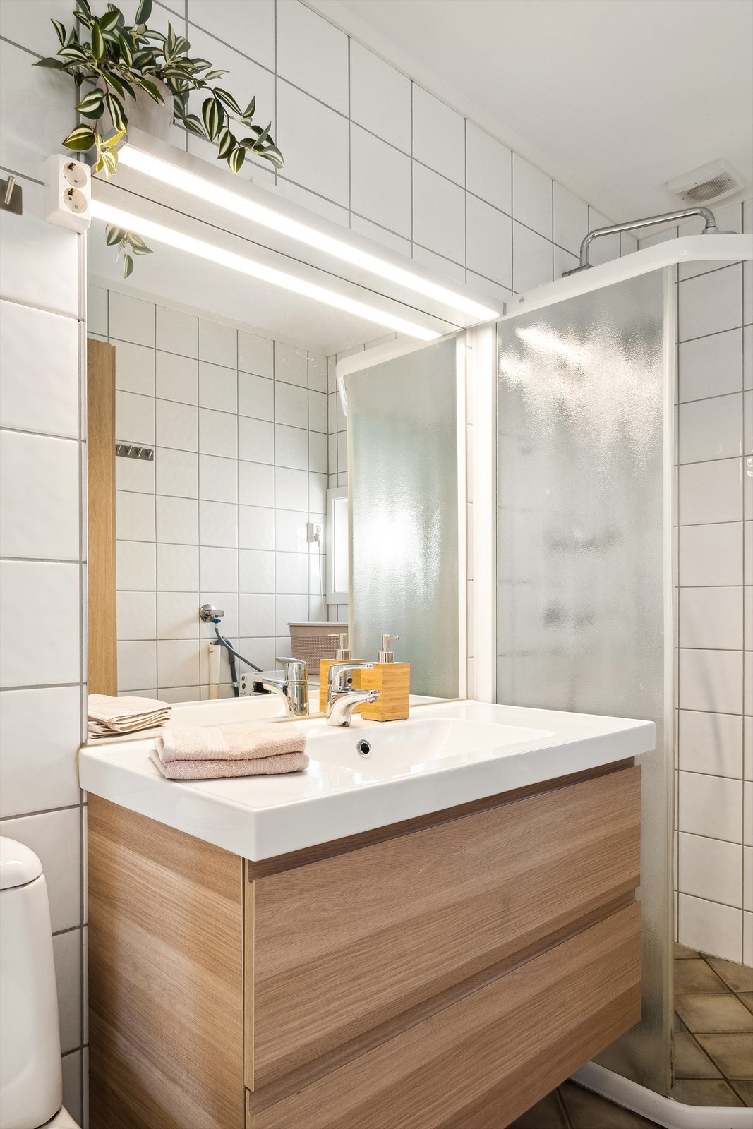 Rommet kombineres med vaskerom og er utstyrt med toalett, dusjhjørne med vegger, heldekkende servant på skuffeinnredning med speil og lys over samt opplegg for vaskemaskin Galleribilde