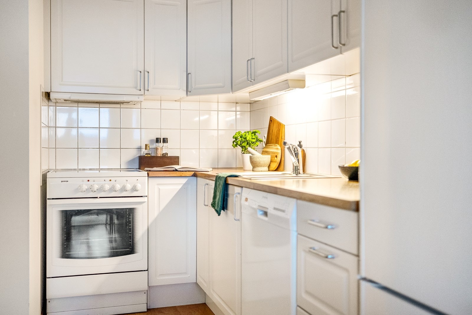 Kjøkkeninnredning med profilerte fronter. Laminat benkeplate med nedfelt vask-og skyllekum. Fliser og belysning over benkeplaten. Overskap. Kjøkkenventilator via mekanisk anlegg. Galleribilde