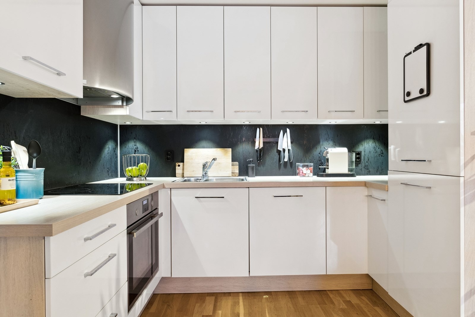 Kjøkkenet har en praktisk U-form med hvite, slette fronter, mørk laminat benkeplate og godt med oppbevaringsplass. Integrerte hvitevarer som kombiskap, oppvaskmaskin, platetopp og stekeovn følger med. Galleribilde