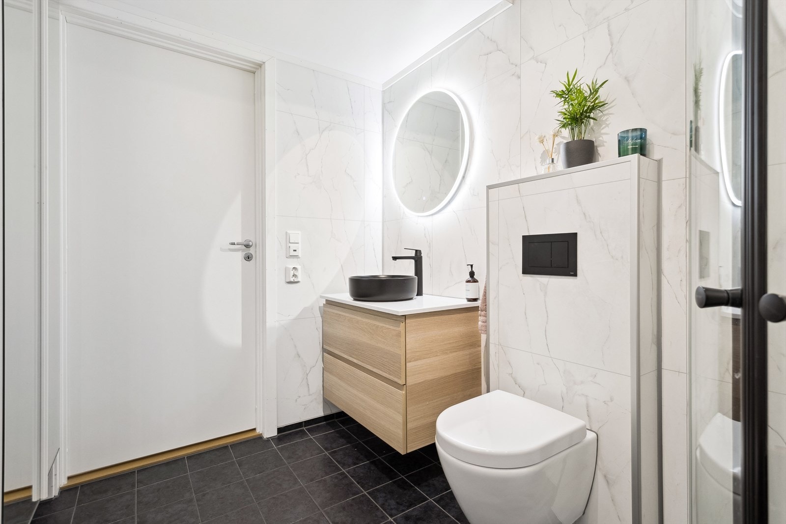 Badet er flislagt og har varme i gulvet, dusjvegger i glass, vegghengt toalett og opplegg for vaskemaskin. Galleribilde