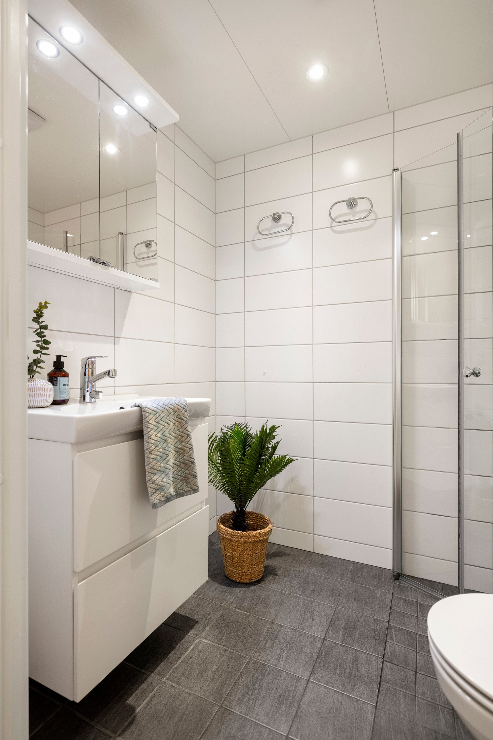 Badet er lyst og flislagt fra 2019 med vannbåren gulvvarme og inneholder vegghengt toalett, servant med skuffer og en dusjløsning med innad slående dører. Galleribilde