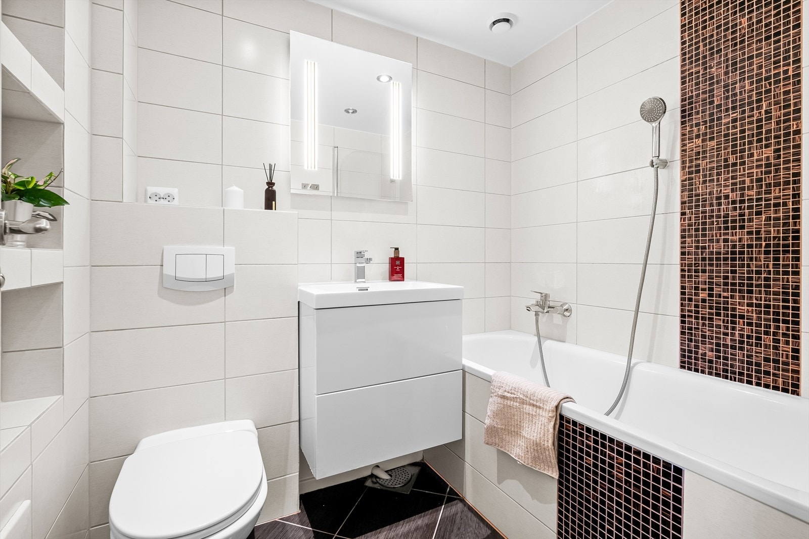 Baderomsinnredning bestående av benkeskap med glatte fronter, servant i helstøpt plate med speil og belysning. Innfliset badekar med dusj og veggfestet klosett med innebygget sisterne. Galleribilde