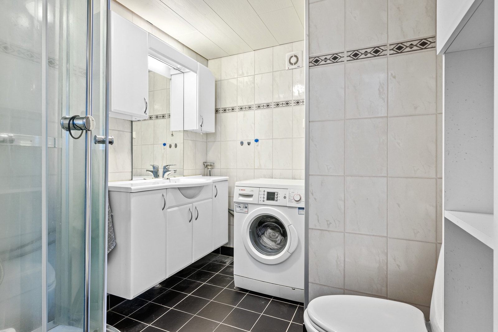 Baderom i 2. etasje med flislagt gulv, gulvvarme, baderomsplater på vegger, dusjkabinett, mekanisk avtrekk, opplegg for vaskemaskin, servantskap og wc. Galleribilde