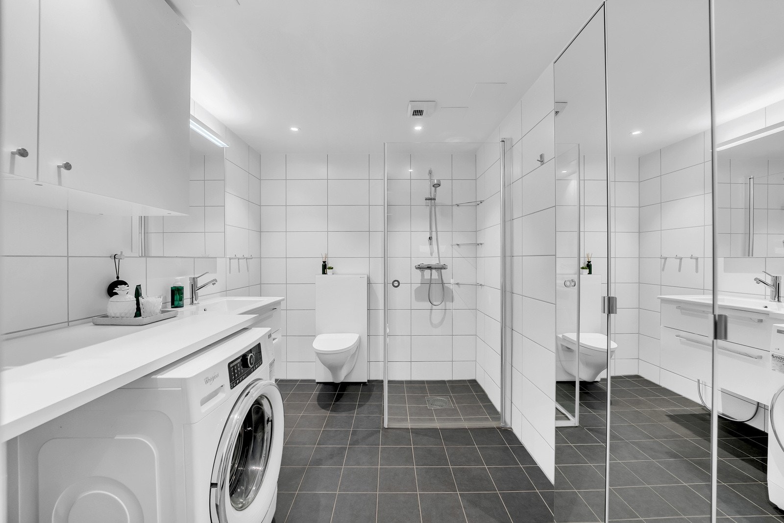 Videre har badet veggmontert toalett, dusjdører i herdet glass på badet, og opplegg for vaskemaskin. Galleribilde