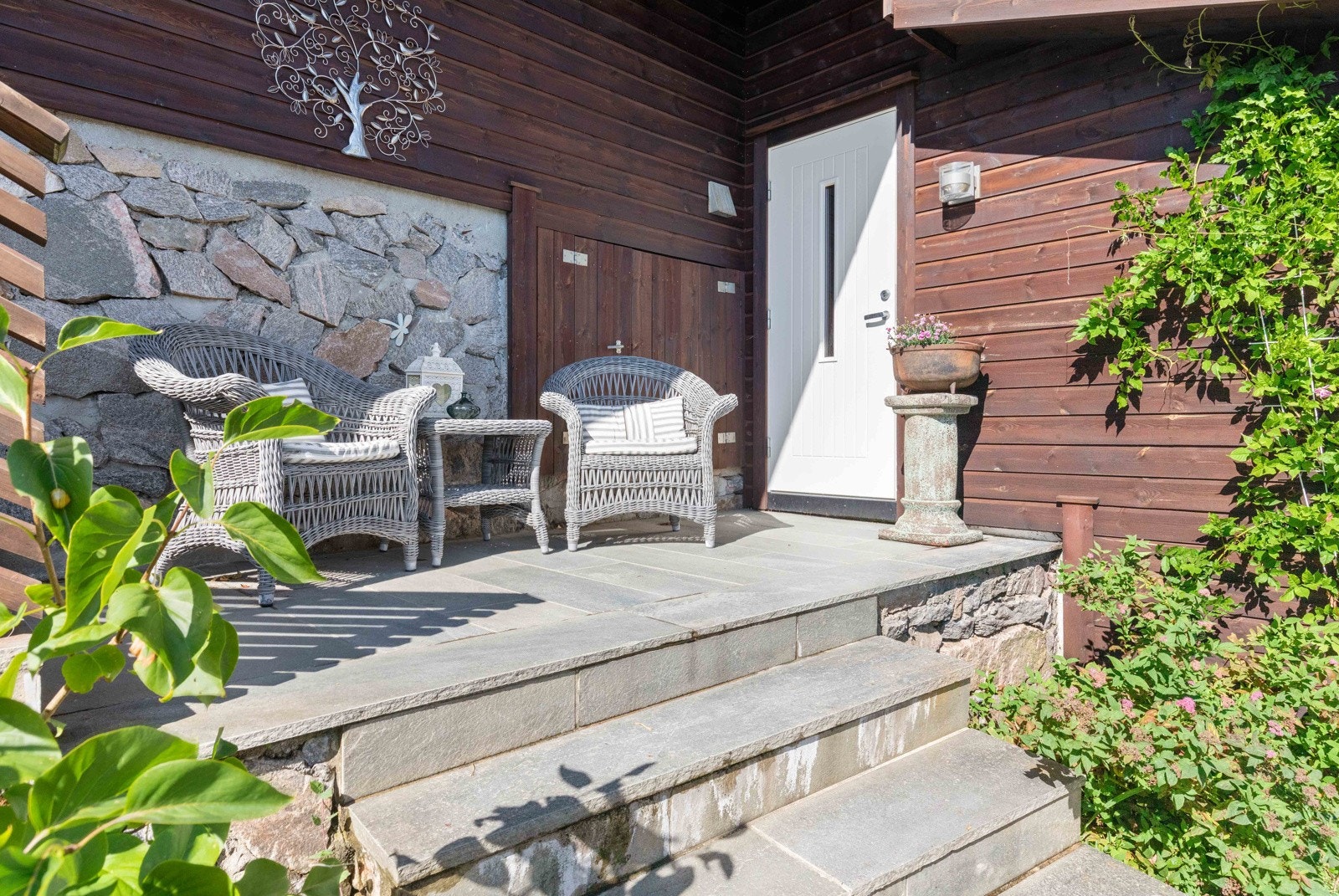 Midtre del av trapp med koselig platting av skifer og inngangsdør til garasje/lagringsplass. Garasje med plass til 2 biler og 2 elbil-ladere. Galleribilde