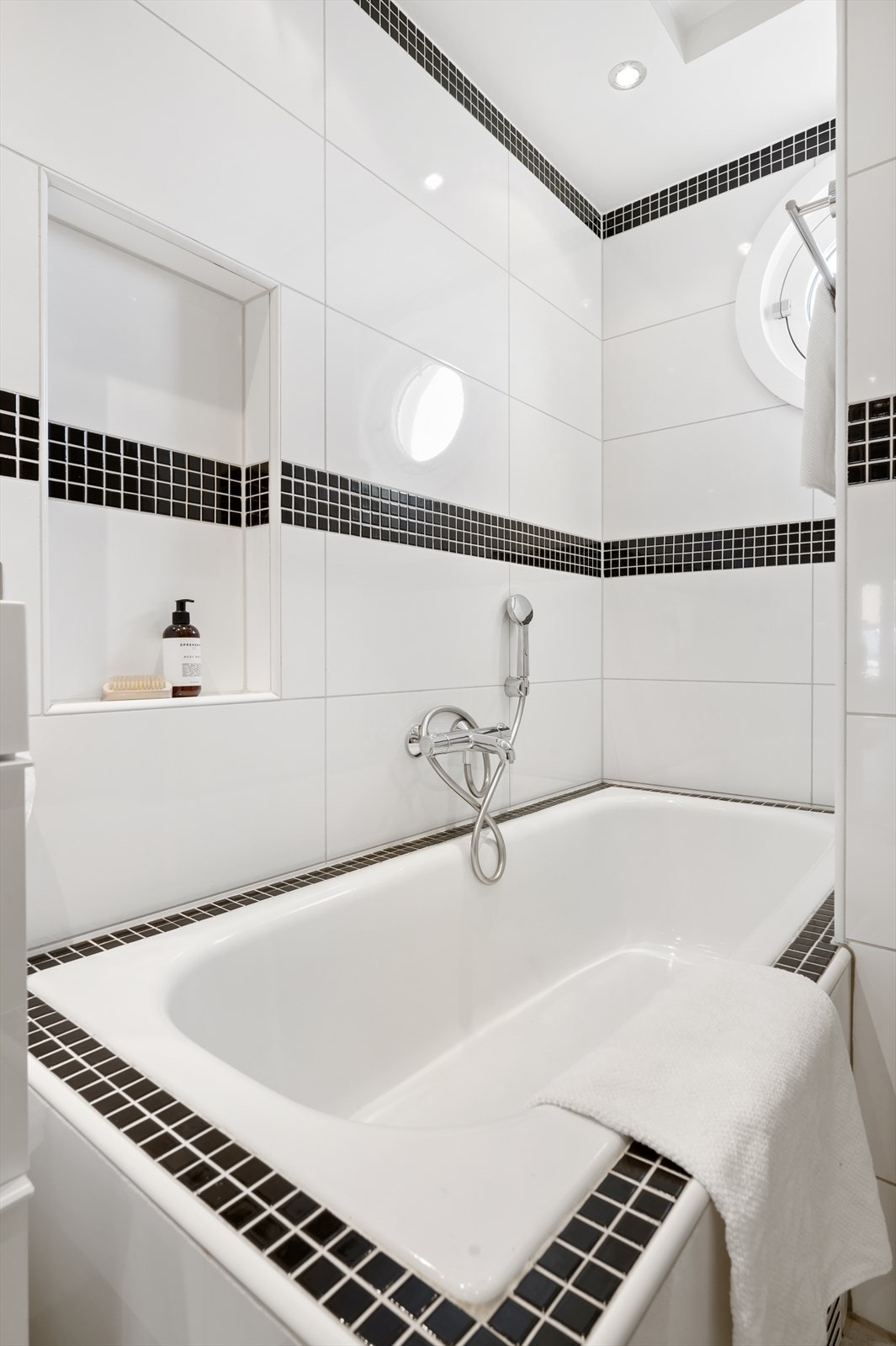 Videre har badet dusjhjørne med glassdører, innebygget badekar og vegghengt toalett med innebygget sisterne. Det er opplegg for vaskemaskin og tørketrommel i mellomgangen foran badet. Galleribilde