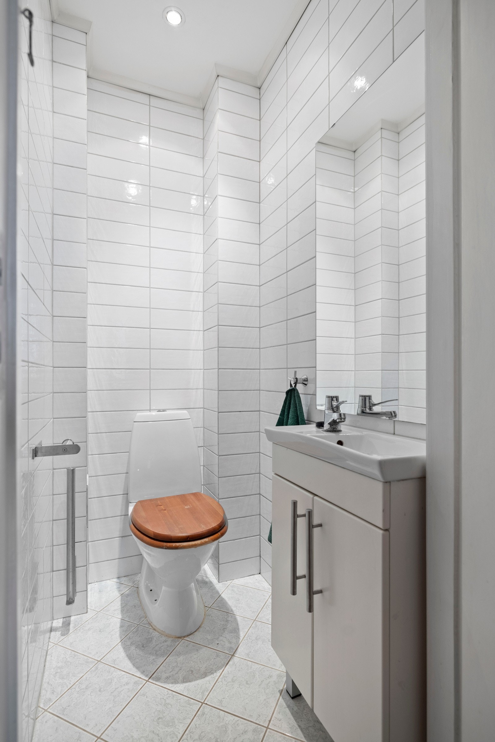 Toalettrom med veggmontert servantskap med keramisk vask og ett-greps armatur i krom, gulvstående klosett og innfelte downlights Galleribilde