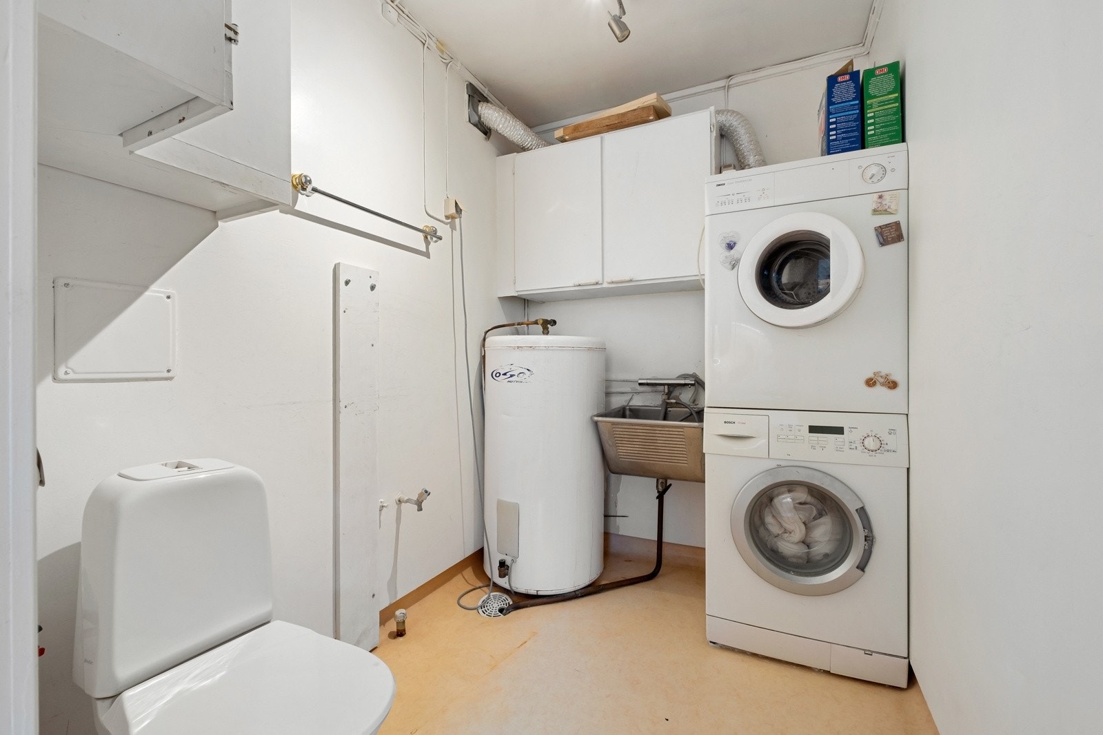 Eldre vaskerom i boligens 2. etasje med belegg på gulv og malte veggflater. Inneholder bla. utslagsvask, toalett, veggskap, samt opplegg for både vaskemaskin og tørketrommel. Det er etablert sluk i gulv. Vaskerommet har behov for oppgradering. Galleribilde