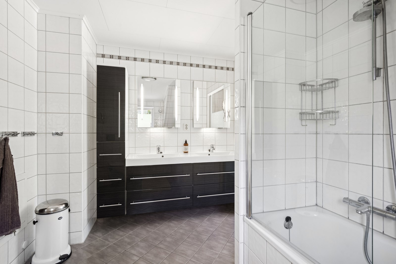 Badet ble pusset opp i 2012. Det er med mørke fliser på gulv og lyse fliser på vegg. Videre er rommet utstyrt med dobbelt servant med underskap, speil, badekar med dusj og vegghengt toalett. Galleribilde