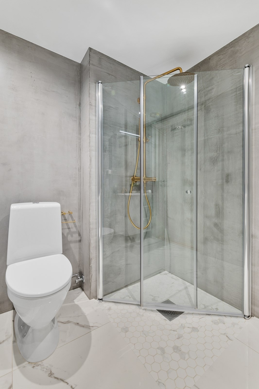 Badet har flotte fliser på gulv og moderne mikrosement på vegger. Badet er innredet med dusjhjørne med takdusj bak svingbare glassdører, gulvstående toalett, servant med underskap samt overskap med speildører og lys. Galleribilde