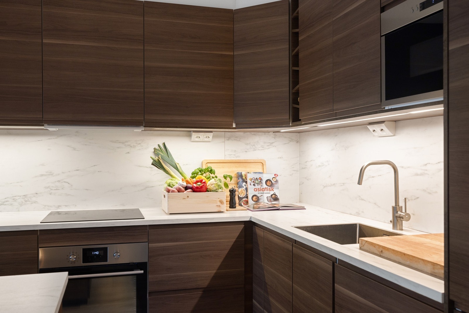 Integrerte hvitevarene som komfyr, induksjonstopp, oppvaskmaskin og kombiskap. Galleribilde