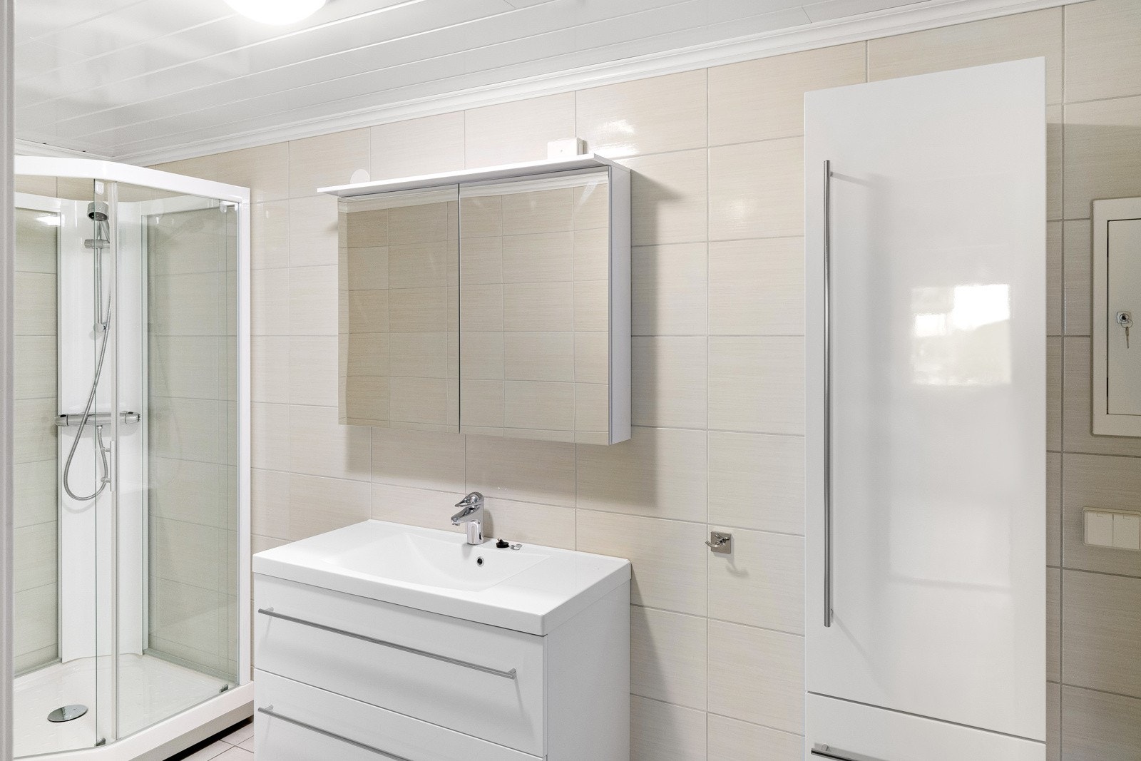 Stilrent bad med dusjkabinett, servant med speilskap og høyt skap. Galleribilde