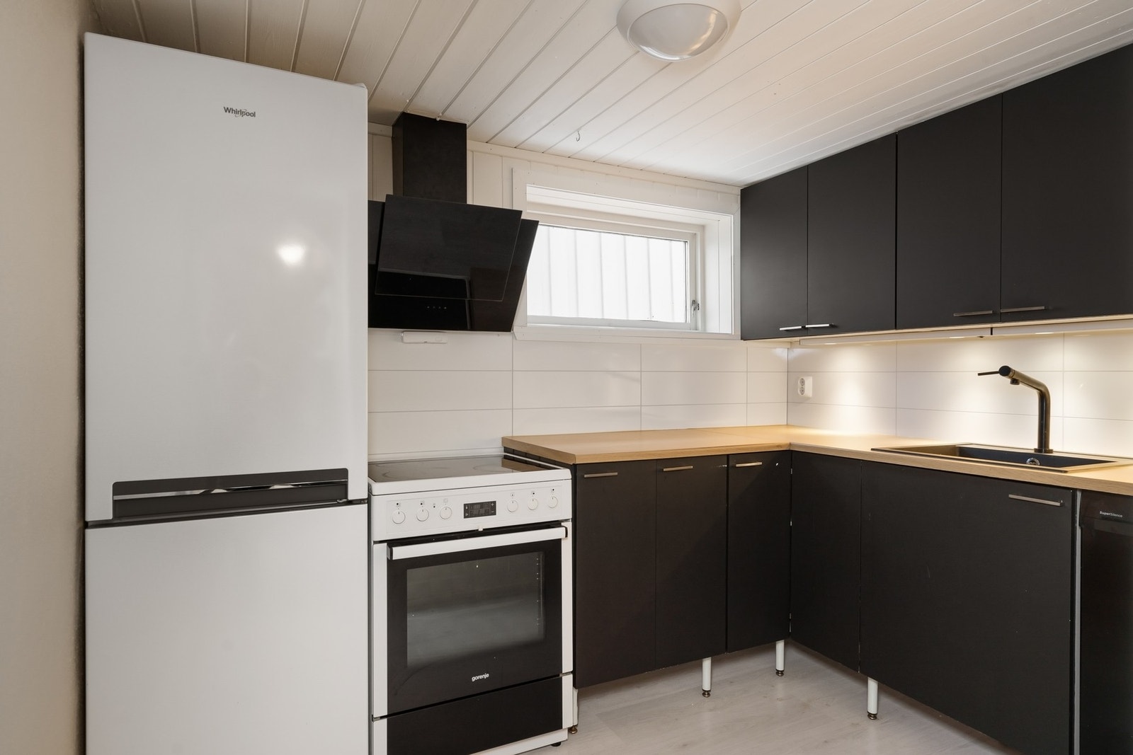 Kjøkken i kjeller har innredning med malte skapfronter i glatt utførelse, og laminert benkeplate. Frittstående hvitevarer. Galleribilde