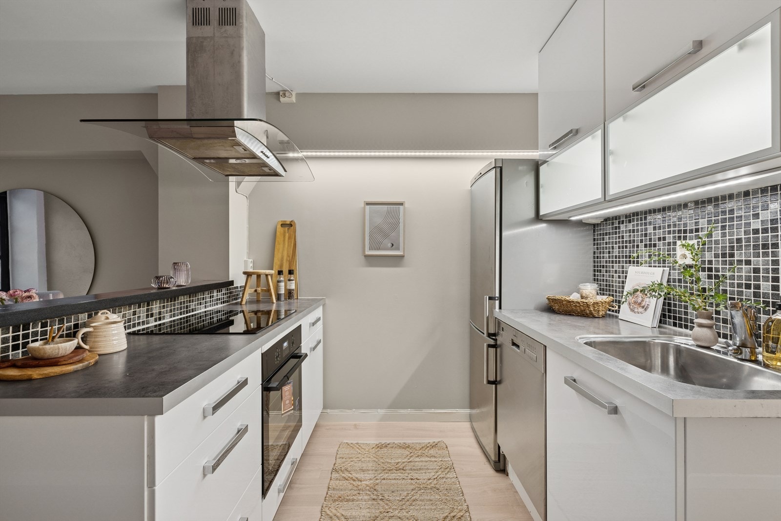 Kjøkkeninnredning med glatte høyglans skapfronter, laminat benkeplate med mosaikkfliser på bakvegg, enkel,oppvaskkum, ventilator og avtrekk over kokesone viakjøkkenventilator med kullfilter. Galleribilde