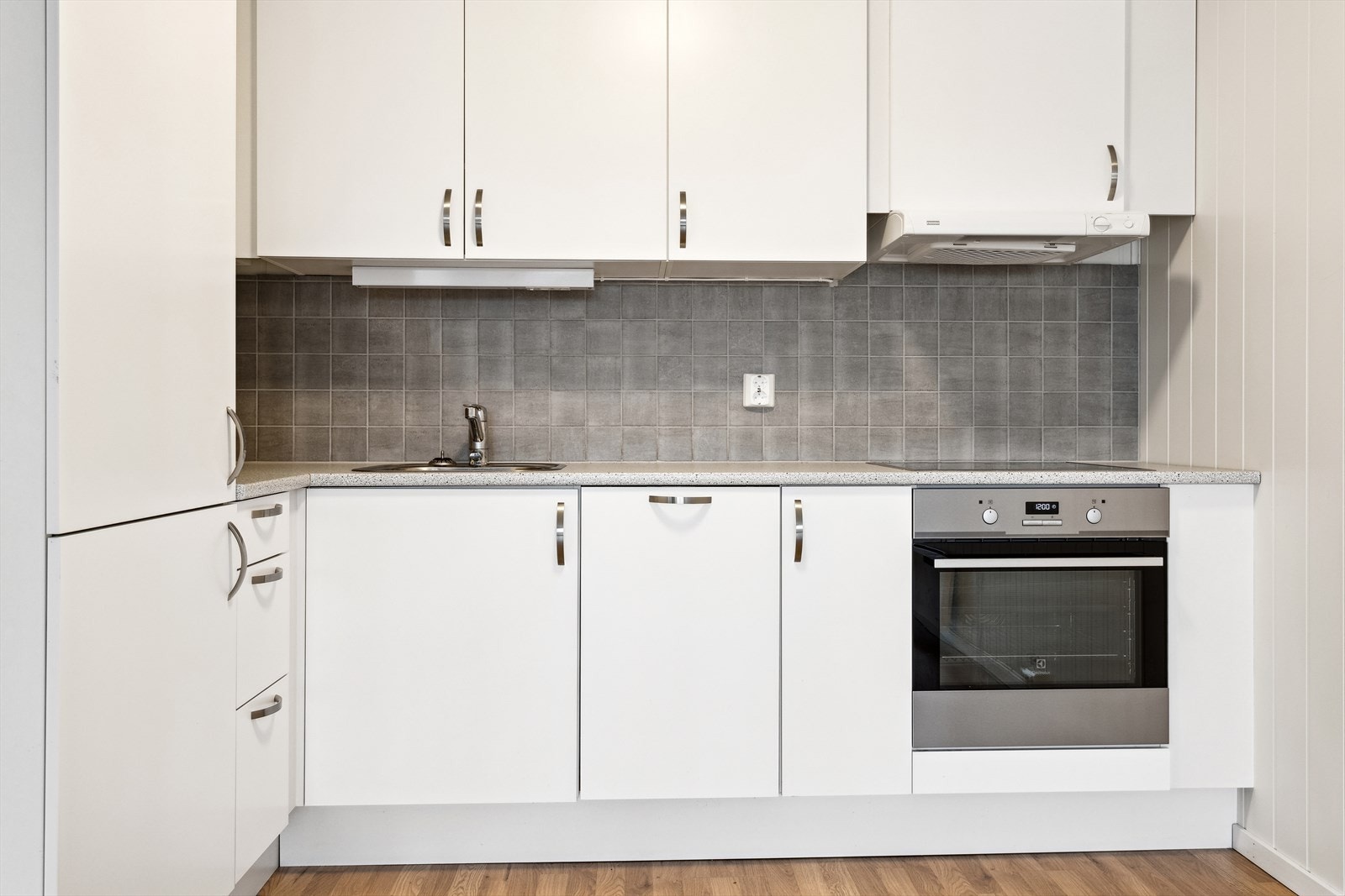 Moderne kjøkken med hvite, glatte fronter, grå fliser over benken og integrerte hvitevarer. Perfekt for både hverdagsmatlaging og større middager. Galleribilde