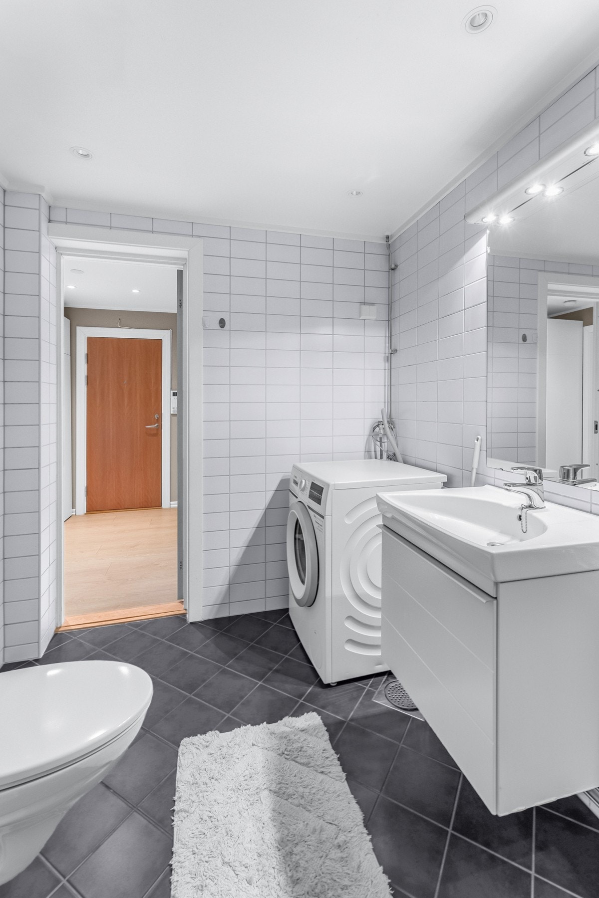 Badet er godt utstyrt med dusjhjørne med skyvedører i glass, vegghengt WC, servantskap og speil med belysning. Det er også opplegg for vaskemaskin, som gjør hverdagen litt enklere. Galleribilde