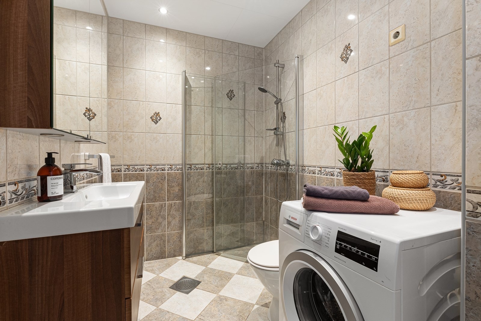 Flislagt bad med lyse flis- og materialvalg. Dusjnisje med innfellbare glassdører og varmekabler i gulv. Galleribilde