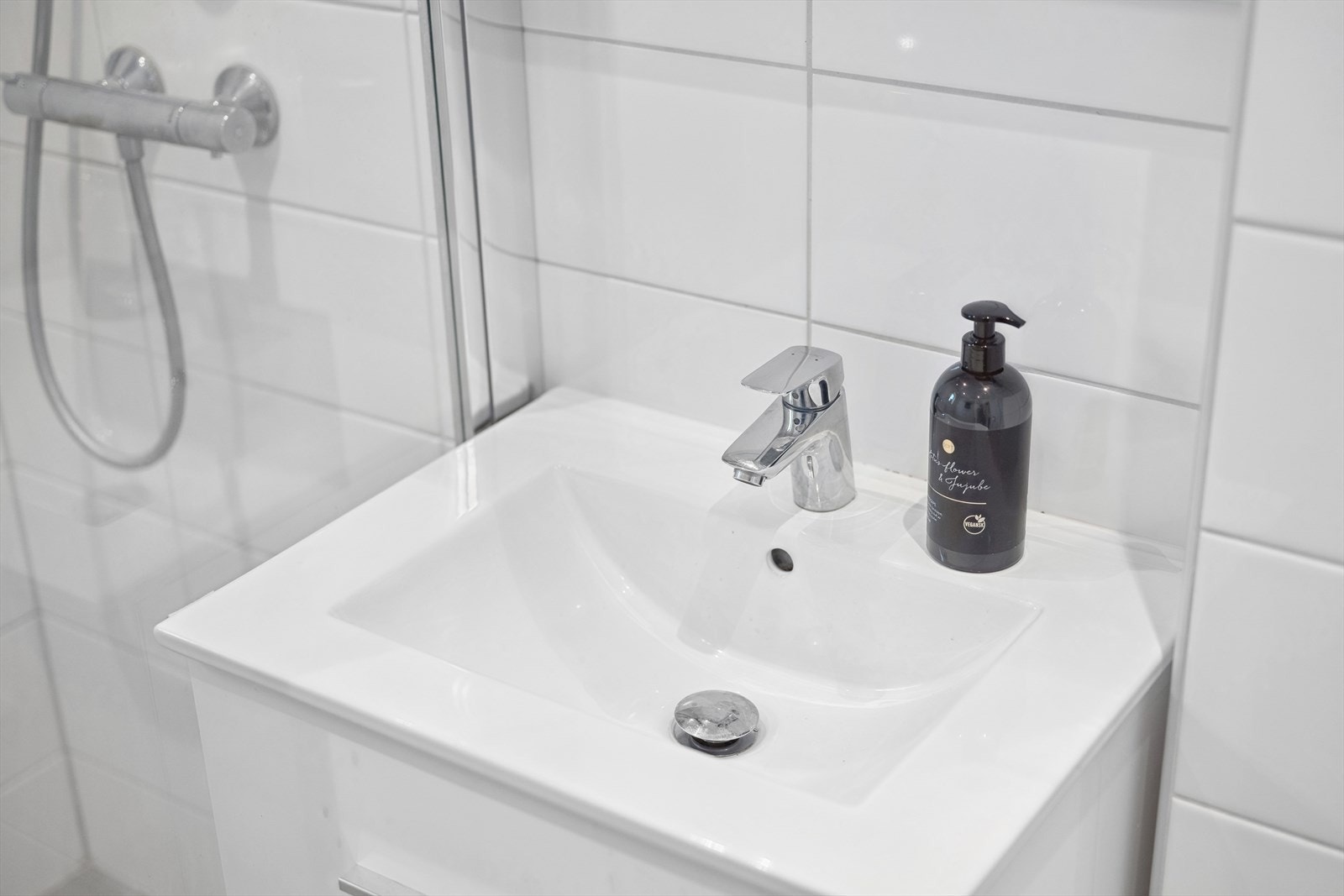 Her er det helflislagt med mørke fliser på gulv og hvite fliser på vegger. Badet er innredet med en servant med underskuffer, speil, et vegghengt toalett og dusjhjørne. Galleribilde