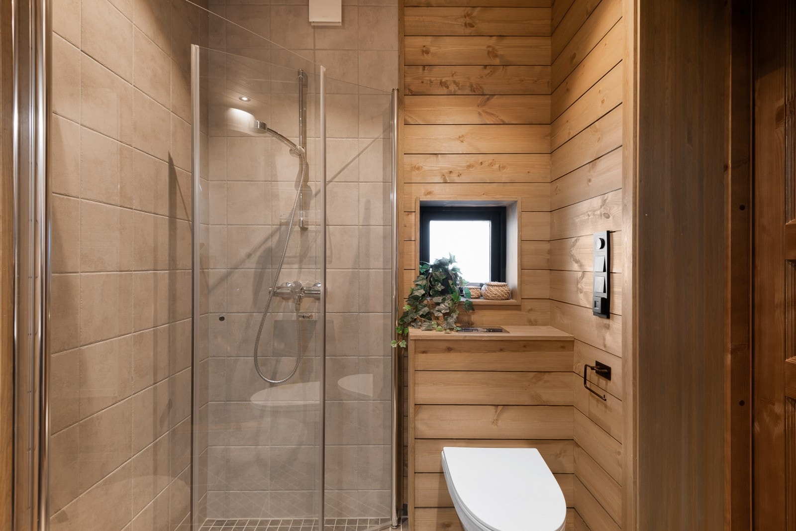 Dusjområdet i hjørnet har innfellbare glassdører og veggmontert dusjsett med hånddusj. Galleribilde