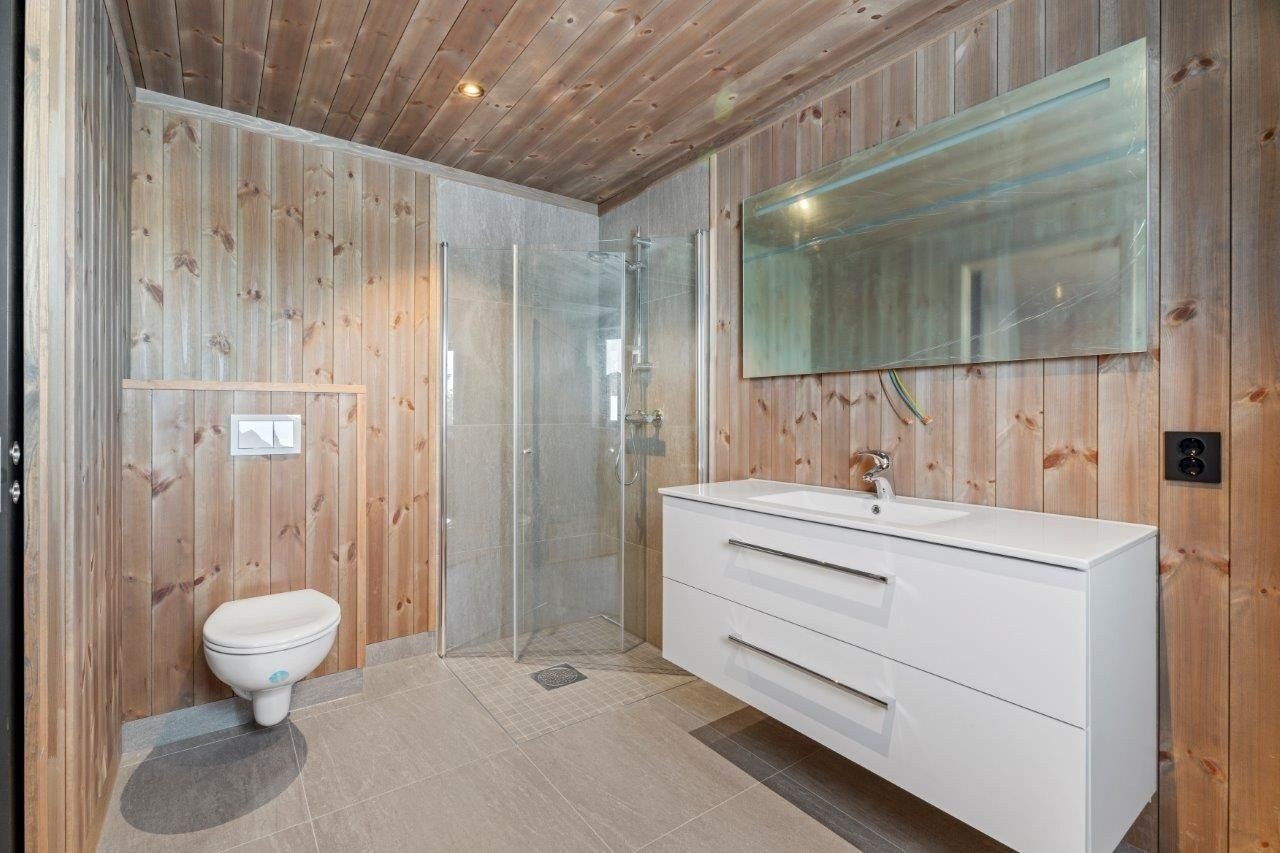 Hytta har to bad. Dette delikate badet er tilknyttet hovedsoverommet og byr på et romslig dusjhjørne, WC og lys baderomsinnredning Galleribilde