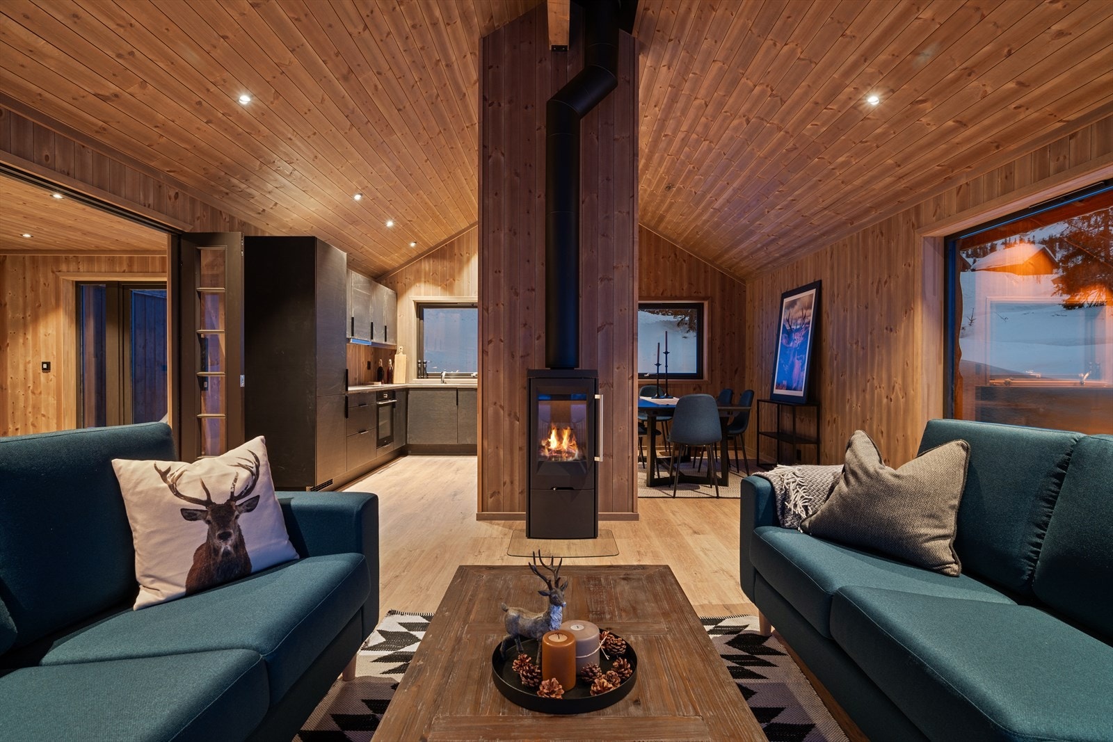 Ringerud Hytteutvikling presenterer en stilren hytte med røstet himling og synlig limtredrager i stuen, som skaper den perfekte hyttestemningen. Vedovnen er strategisk plassert midt i rommet for optimal varmefordeling Galleribilde