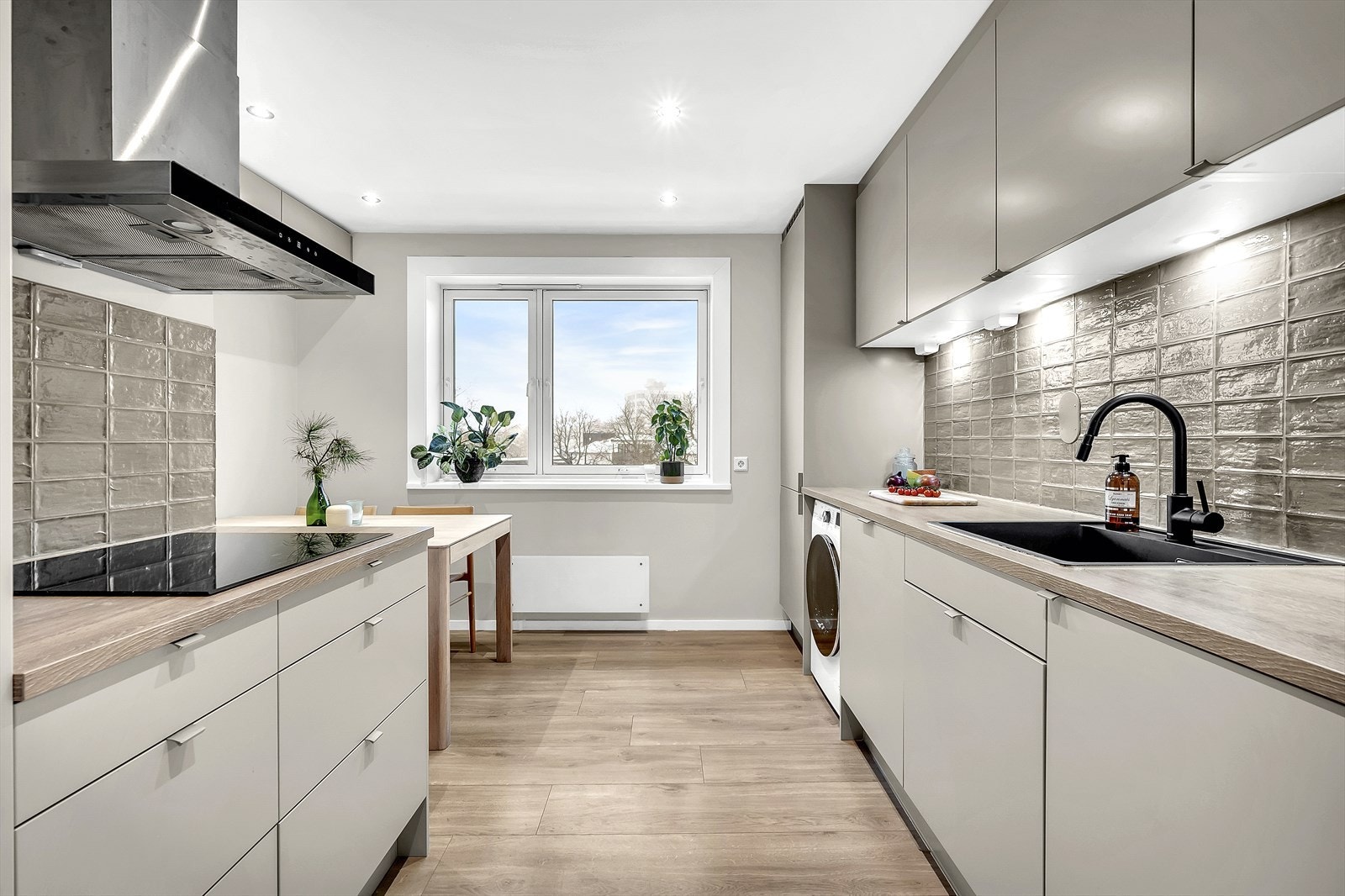 Kjøkkenet har stilrene, glatte fronter i en beige fargetone og en laminatbenkeplate med nedfelt vask. Galleribilde