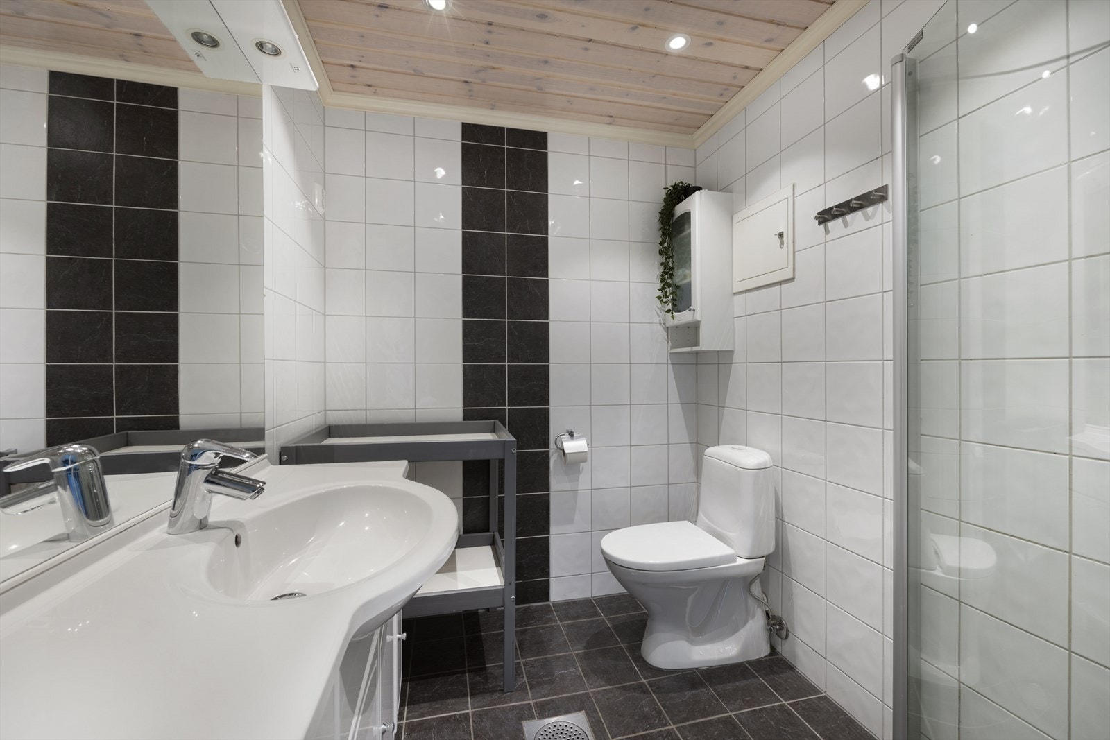 Fint bad med fliser, gulvmontert toalett, heldekkende servant og speil. Badet har også et dusjhjørne med glassdører og opplegg til vaskemaskin. Galleribilde