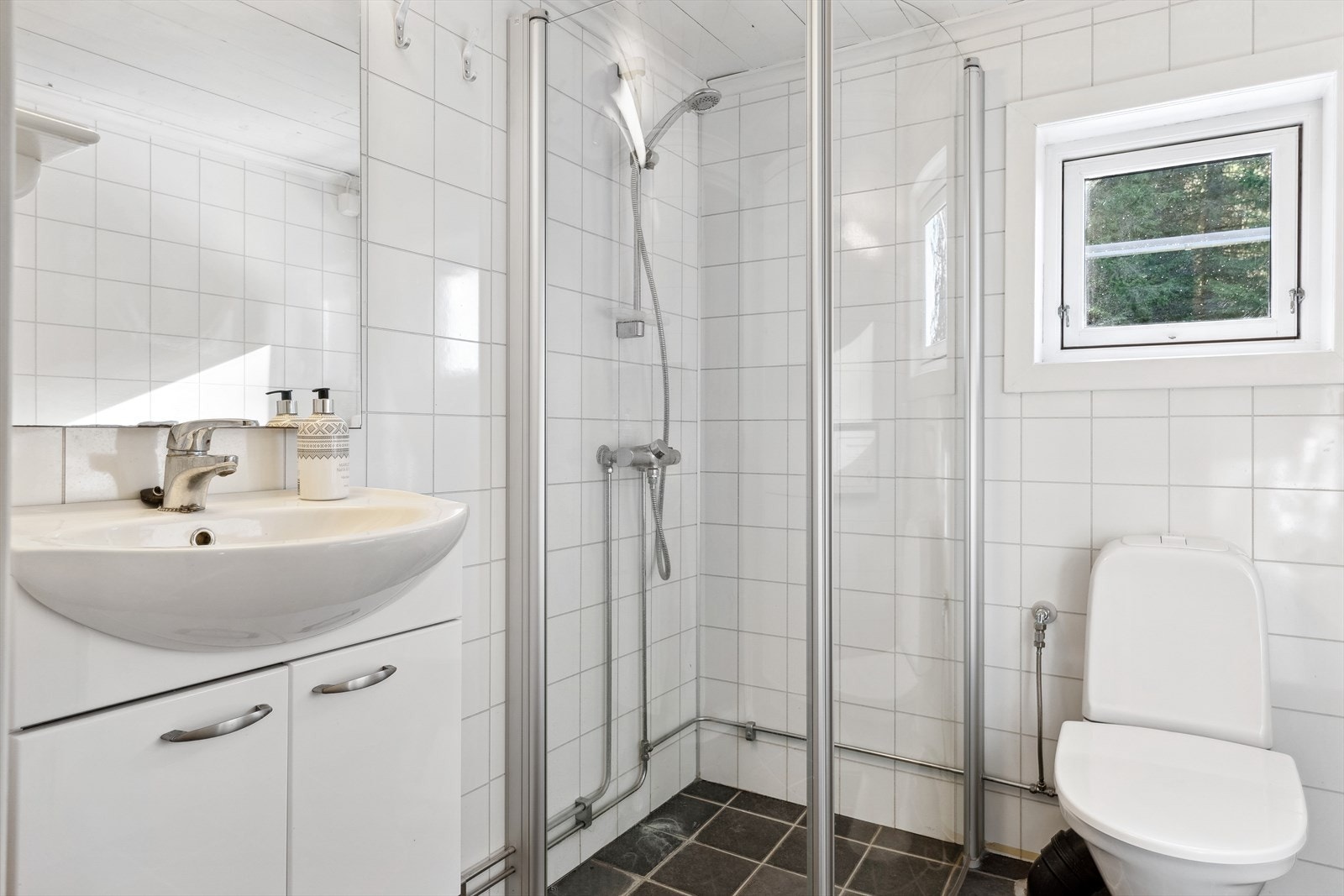Badet har fliser på gulv og våtromsplater på vegg. Innredet med dusjhjørne, wc og baderomsinnredning med servant. Galleribilde