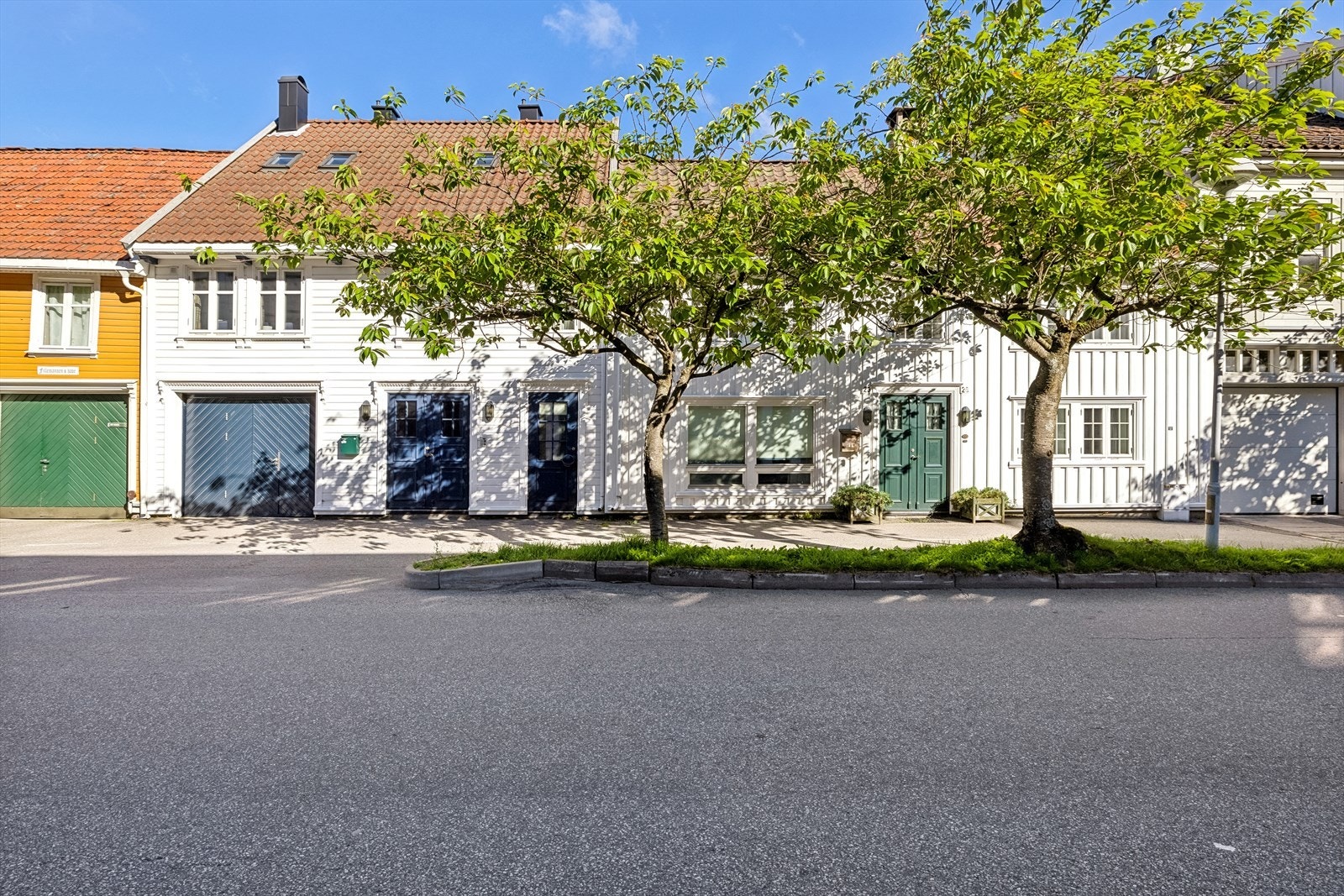 Fra høyre ser man inngang til hovedhus (grønn dør) deretter inngang til butikklokale og hybelhus (blå dører) sist kommer innkjørsel til garasje. Galleribilde