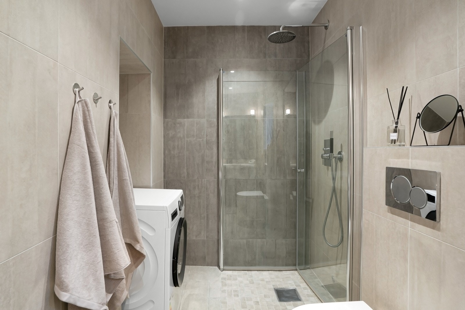 Badet inneholder dusjhjørne med innfellbare dører, vegghengt wc, servant og opplegg for vaskemaskin Galleribilde