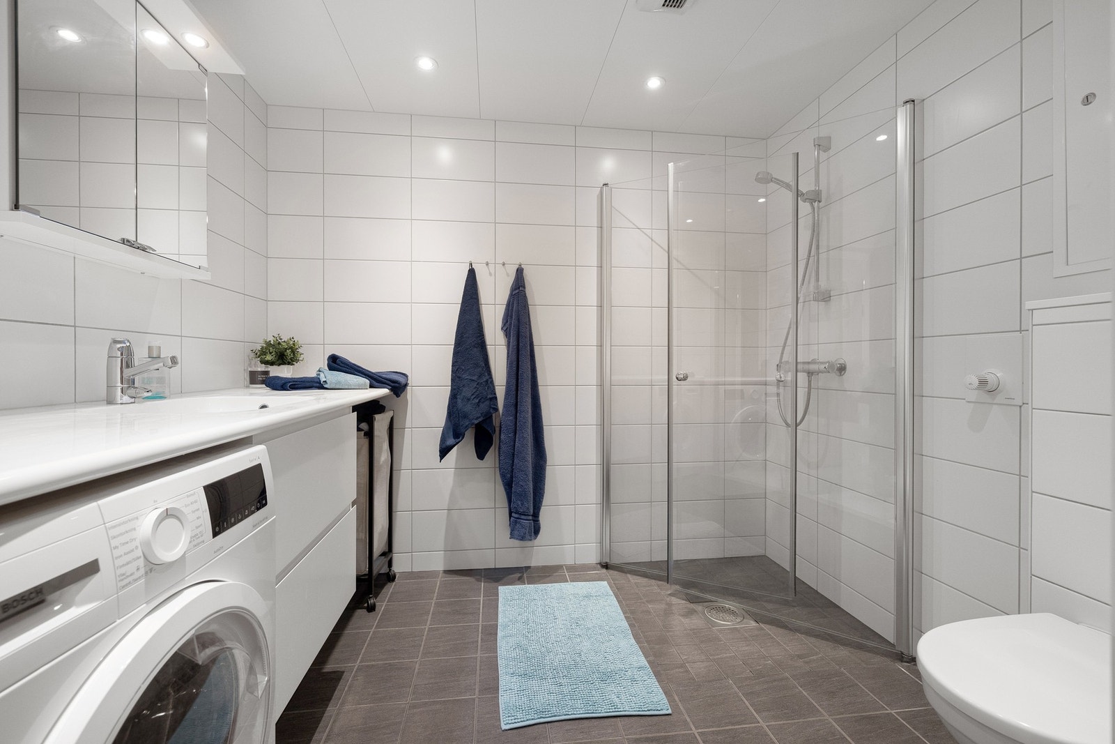 Badet har et stilrent design med flislagte overflater, behagelig vannbåren gulvvarme med termostatstyring og moderne LED-downlights som gir godt lys. Galleribilde