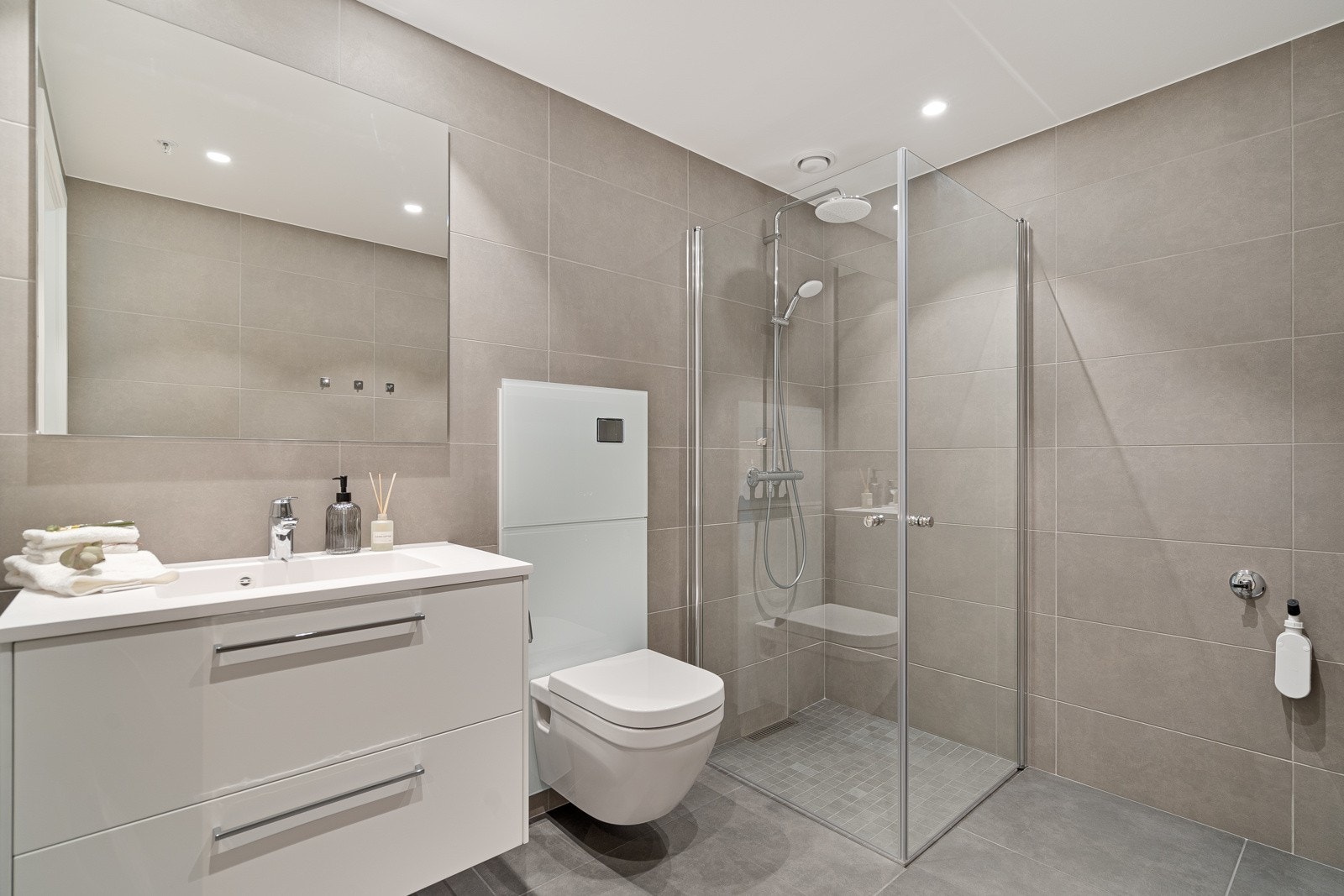 Nydelig flislagtr bad med stor dusjnisje, vegghengt toalett og servant med skuffer og speil Galleribilde