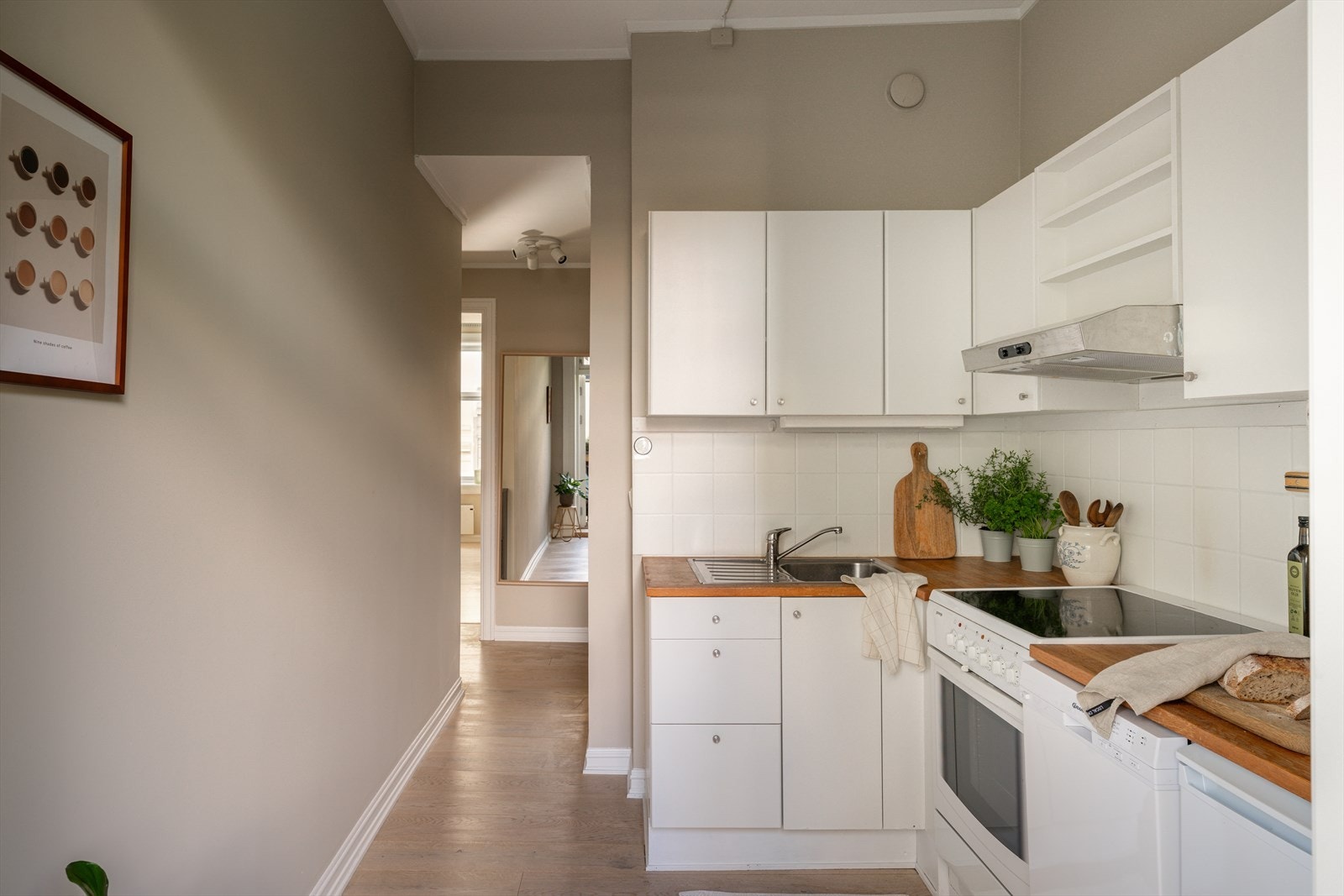 Lyst og stilrent kjøkken med benkeplate i tre utstyrt med frittstående komfyr, kjøleskap og oppvaskmaskin. Galleribilde