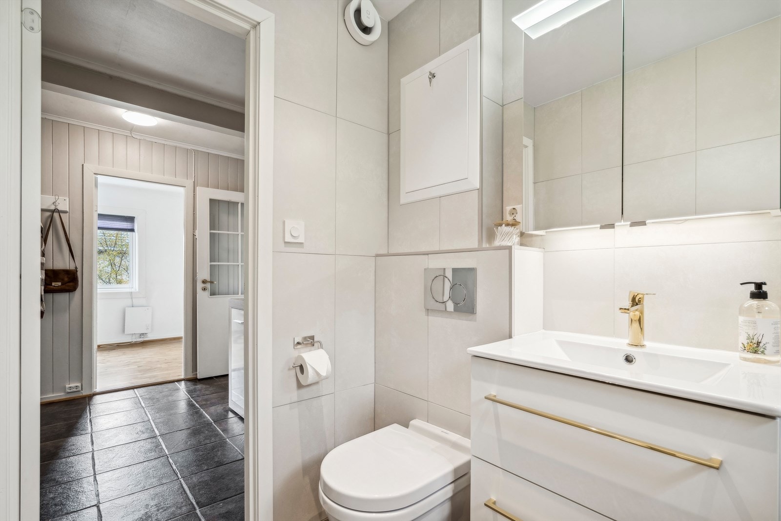 Rommet er utstyrt med en pen servantinnredning med gulldetaljer, speilskap, toalett og dusjhjørne med glassvegg. Galleribilde